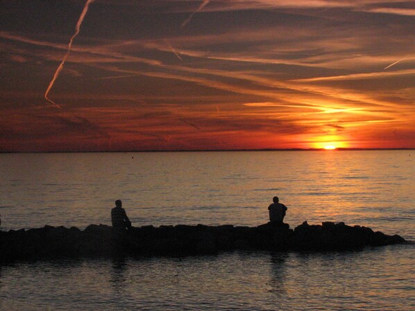 A sunset over a calm sea with two silhouetted figures on a rocky outcrop. - 200 steps to the beach! (Rock Hall)