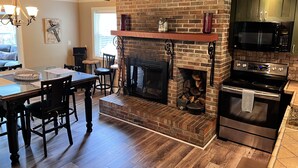 A kitchen with a brick fireplace, wooden flooring, a dining area with a table and chairs, and a modern microwave. - Breathtaking Country Paradise with hot tub  where you can unplug in nature  (Beechgrove)