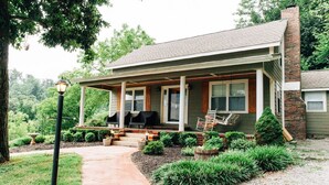 A two-story house with a covered porch, a brick chimney, and a well-maintained front yard with a pathway leading to the entrance. - Breathtaking Country Paradise with hot tub  where you can unplug in nature  (Beechgrove)
