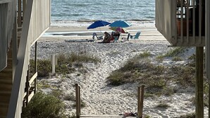 Blick auf einen Strand mit einer Holzterrasse, feinem Sand und einigen Sonnenschirmen.