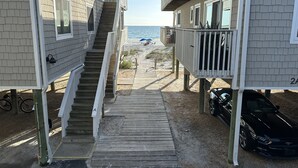 Eine Holztreppe führt zu einem Strand, in dessen Nähe ein Auto geparkt ist.