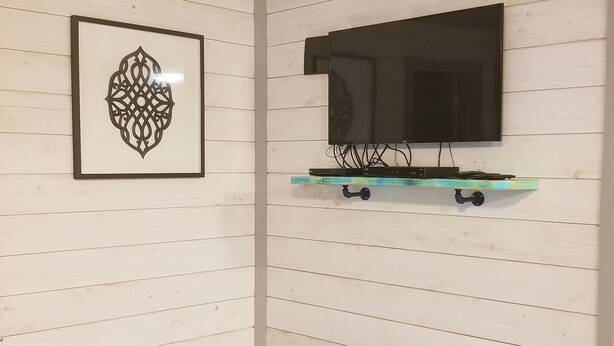 Habitación de esquina con paredes blancas, paneles decorativos y un televisor de pantalla plana montado en un estante color turquesa.