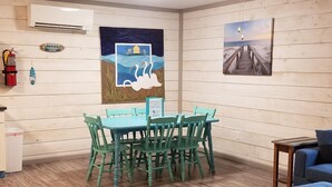 Un comedor con mesa y sillas, un extintor, un cartel de bienvenida y decoración en la pared.