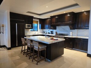 A modern kitchen with dark cabinetry, a marble countertop, a central island with bar stools, and built-in appliances.