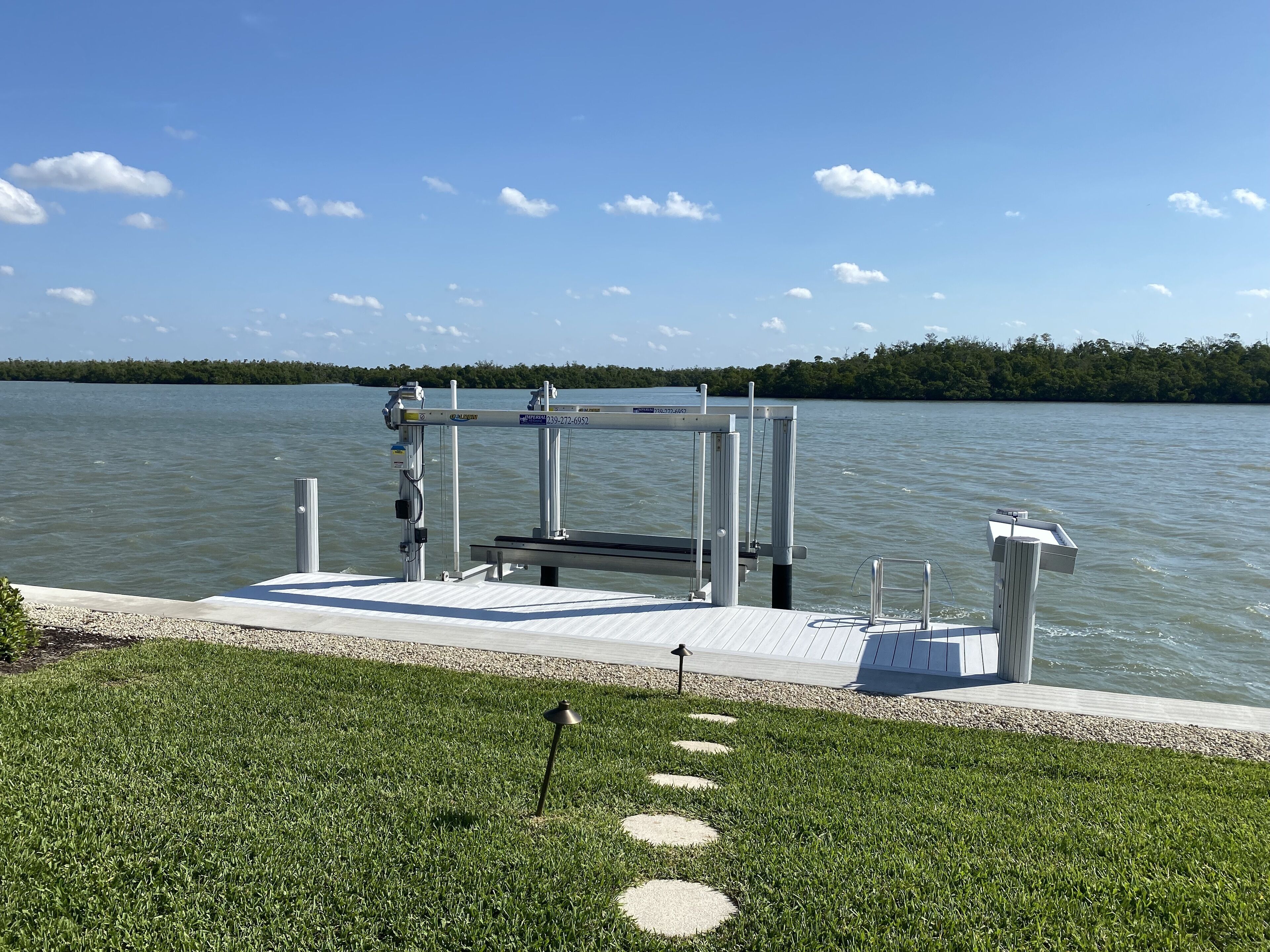 A dock with a metal railing and a bench, surrounded by a grassy area with stepping stones.