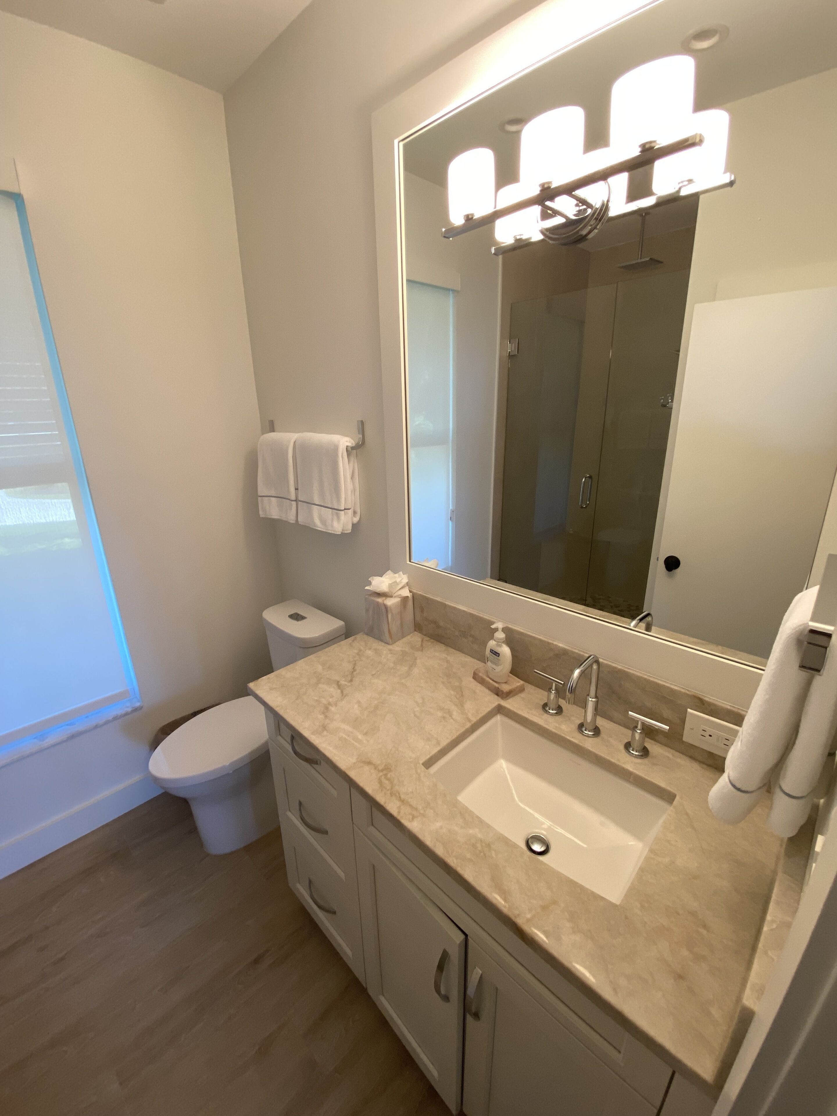 A modern bathroom with a marble sink, a large mirror, and a glass shower enclosure.
