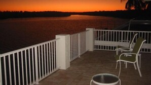 Un balcone con vista su un tramonto sull'acqua, ringhiere bianche e due sedie verdi.