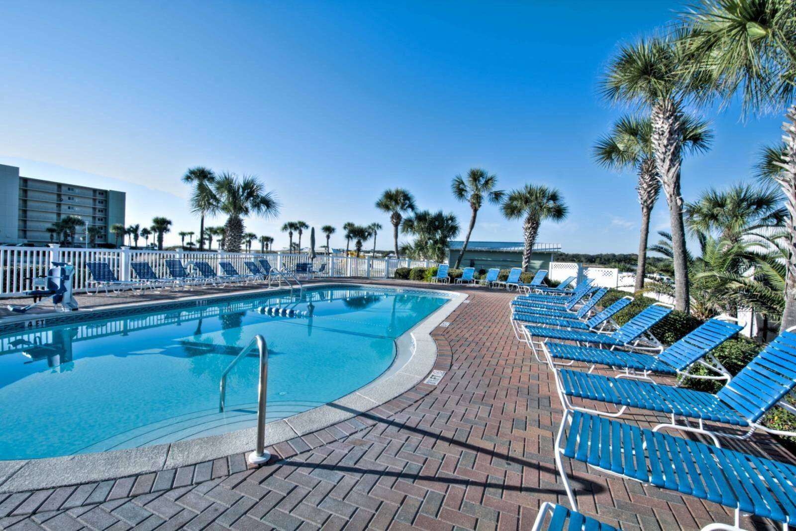 A swimming pool with blue lounge chairs and palm trees.