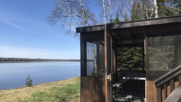 Una cabaña de madera con puerta y ventana de vidrio, con vista a un lago.