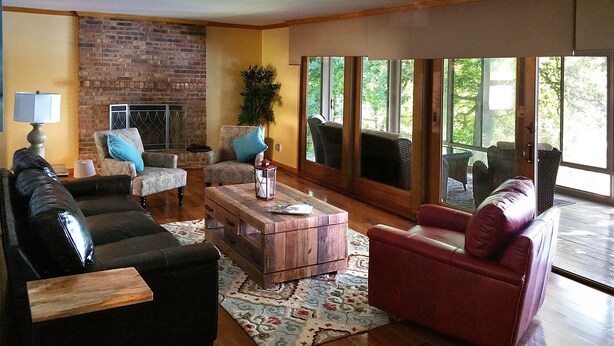 A living room with a brick fireplace, two sofas, a coffee table, and large windows offering a view of trees. - Secluded Lake Retreat-Exceptional Reviews! (Dowling)