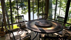 A round table with intricate metalwork, surrounded by four chairs with a lattice back design, set on a wooden deck with a view of a lake through large windows. - Secluded Lake Retreat-Exceptional Reviews! (Dowling)