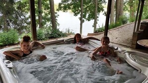 A hot tub with three people sitting in it, surrounded by trees and a view of a body of water. - Secluded Lake Retreat-Exceptional Reviews! (Dowling)