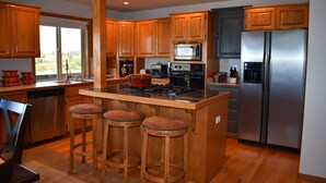 Una cocina moderna con armarios de madera, un refrigerador de acero inoxidable, un microondas y una estufa a gas. Hay tres taburetes de madera en la isla.