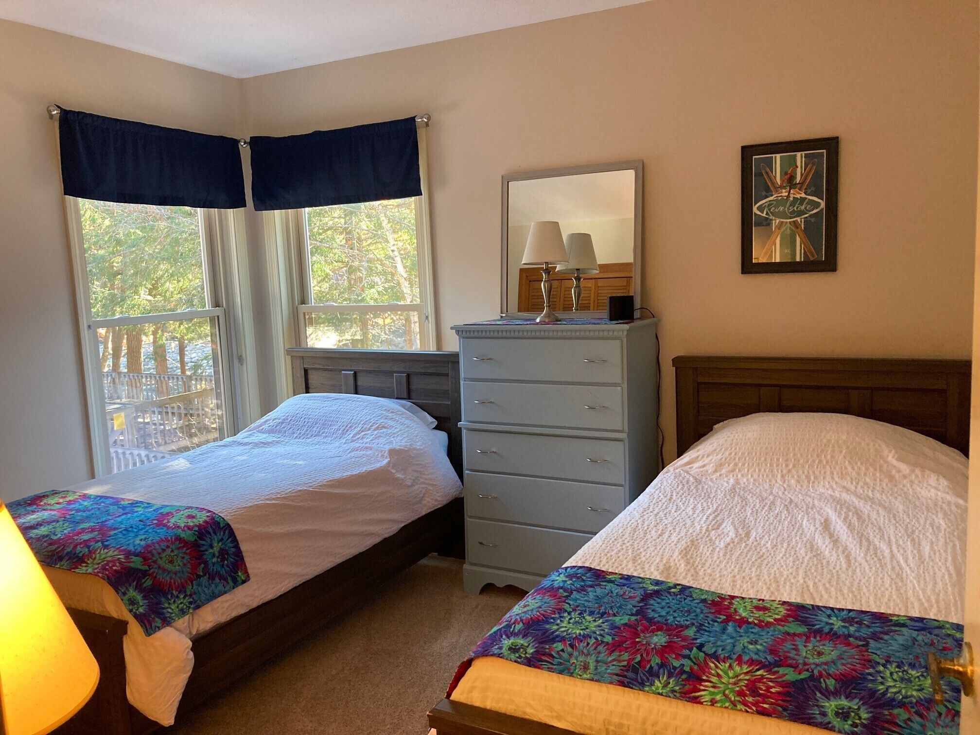 A bedroom with two beds, a dresser, a mirror, and a window with curtains.