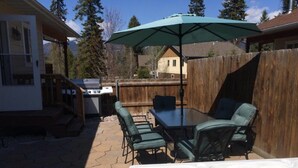 Een terras buiten met een jacuzzi, een tafel met stoelen en een barbecue.