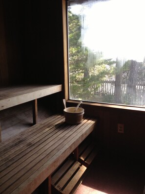 A wooden bench with a rustic design, positioned next to a window with a view of a wooden fence and trees.
