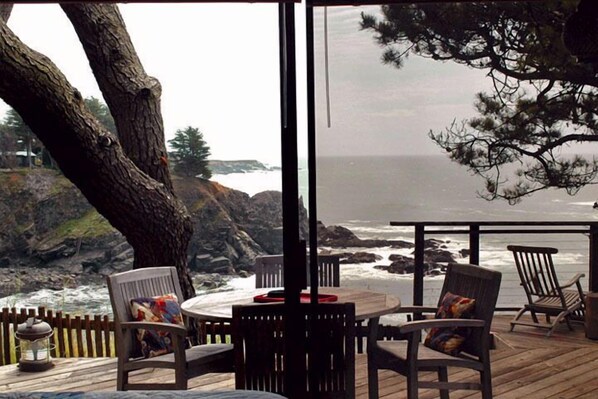 A wooden deck with a table and chairs overlooking a rocky coastline.