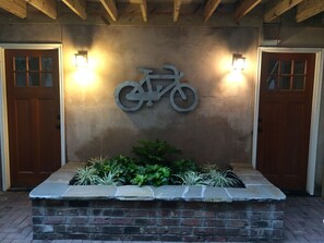 Una zona di accoglienza con un fioriere in pietra, due porte in legno e un simbolo di bicicletta fissato al muro.