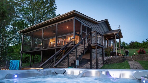 Een modern huis met een glazen terras en een jacuzzi op de voorgrond, met een trap die naar het terras leidt.