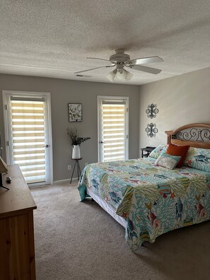 Une chambre à coucher avec un lit, deux portes équipées de stores, un ventilateur de plafond et une petite plante.