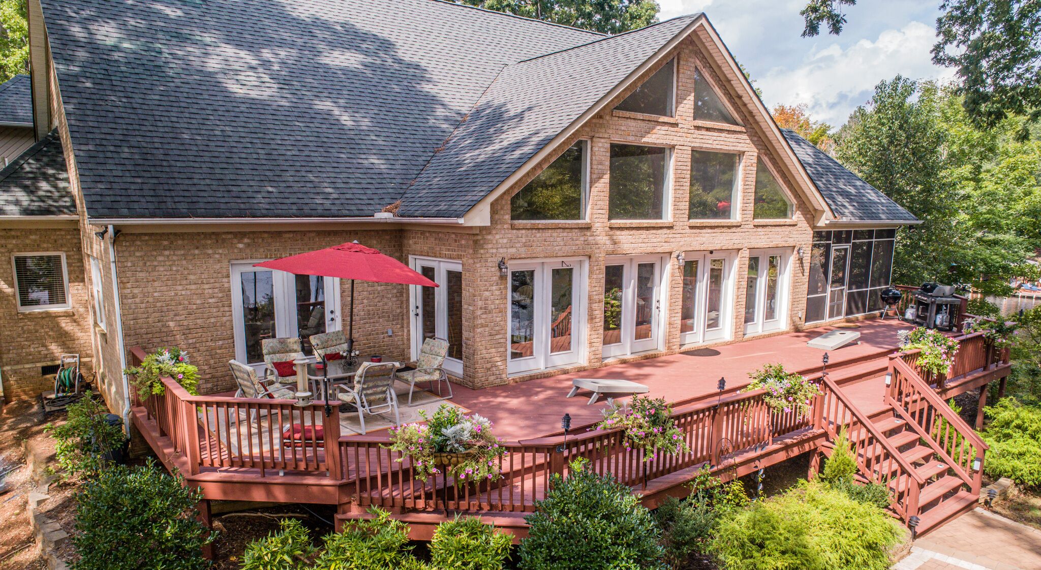 Ein großes Ziegelhaus mit  überdachter Terrasse, Gartenmöbeln und einer Holzterrasse.