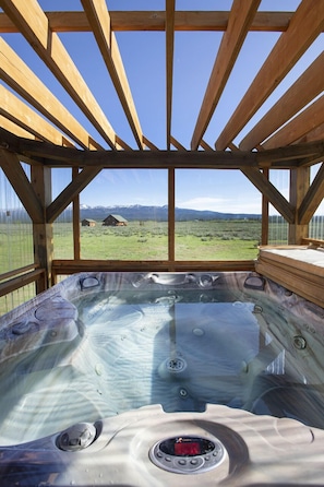 Un jacuzzi con estructura de madera y vista a un campo cubierto de césped y montañas.