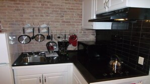A kitchen with white cabinets, a black countertop, and a brick wall. - SPACIOUS AND OPEN PROPERTY W/KITCHEN - 3 MINUTES TO SUBWAY (New York)