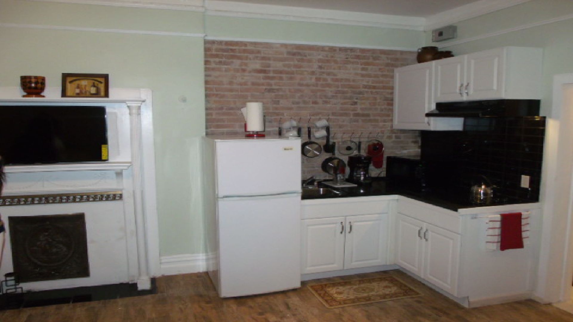 Cocina compacta con armarios blancos, refrigerador, microondas y pared de ladrillo.