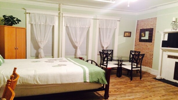 A bedroom with a bed, a small table with chairs, a wooden wardrobe, and a brick wall. - SPACIOUS AND OPEN PROPERTY W/KITCHEN - 3 MINUTES TO SUBWAY (New York)