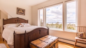 Ein Schlafzimmer mit einem hölzernen Bett, einem großen Fenster mit Aussicht und einem Koffer auf dem Boden.
