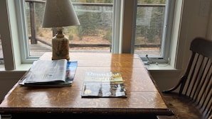Ein Holztisch mit einer Lampe und Zeitschriften, ein Fenster mit Blick auf Bäume und ein Gewässer.