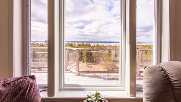 Ein Zimmer mit großem Fenster und Blick auf bewaldetes Gelände sowie ein Gewässer.