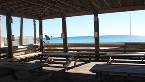 A wooden deck with picnic tables and a view of the ocean. - BEACH COTTAGE 3BR , GOLF CART W/HOUSE, PORCH SWING ,POOL 30 STEPS AWAY, PETS LOV (Destin)