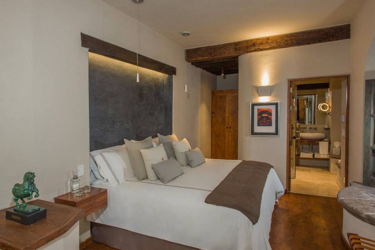 A bedroom with a large bed, bedside tables, a wooden headboard, and a bathroom visible through an open door.