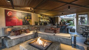Un espace de détente moderne doté d’un foyer, de sièges agrémentés de coussins, d’un bar avec des bouteilles et d’une vue sur l’extérieur.