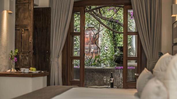 Une chambre dotée d’une grande fenêtre, de meubles en bois et offrant une vue sur la verdure environnante.