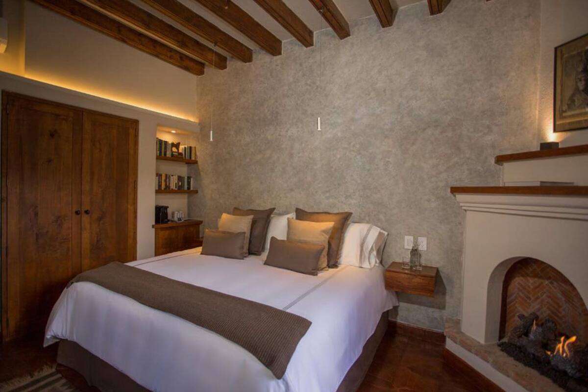 A bedroom with a large bed, wooden beams, a fireplace, and a bookshelf.
