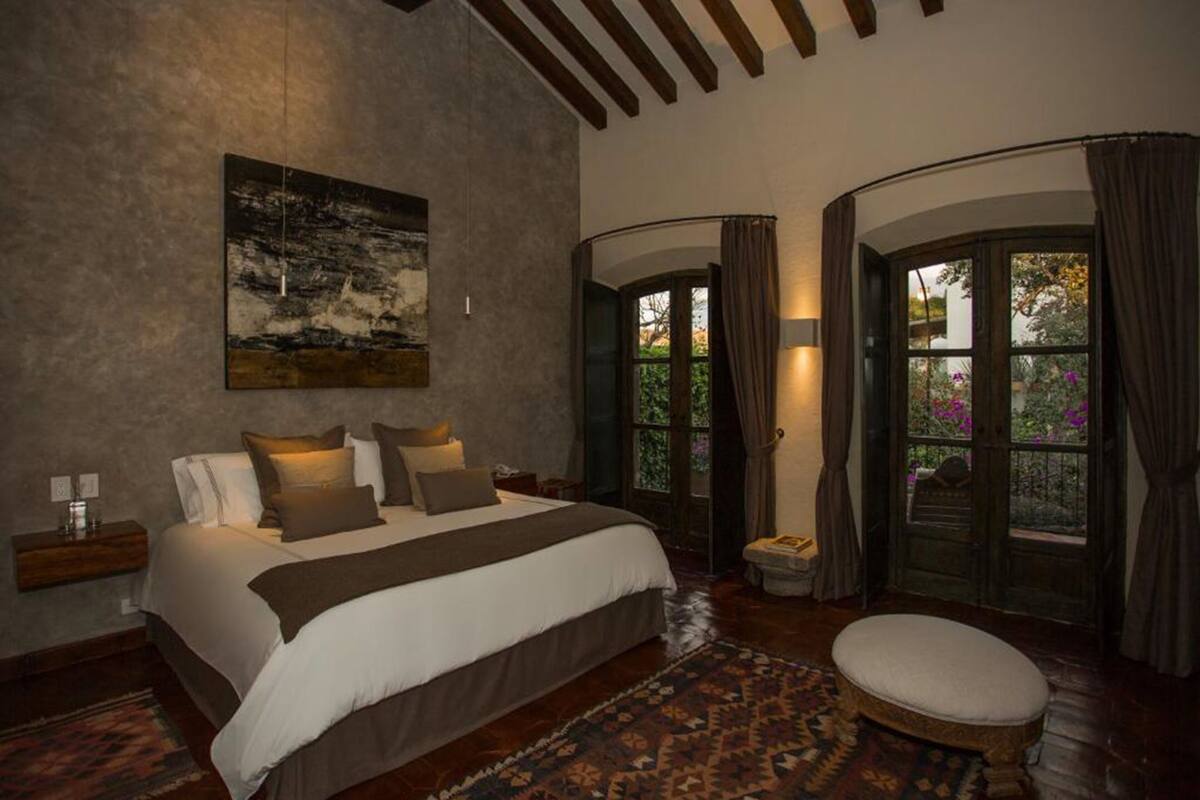 A bedroom with a large bed, a nightstand, a rug, and a window with curtains.