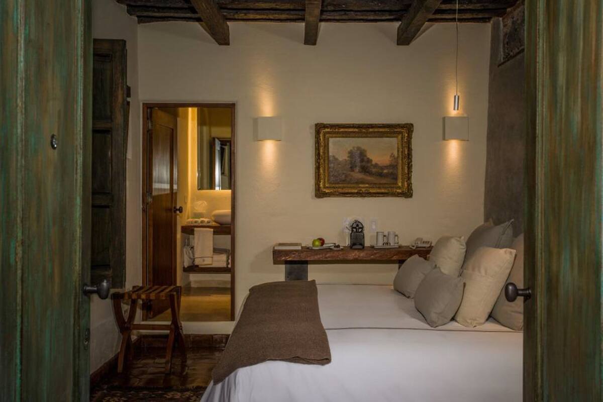 A bedroom with a bed, a nightstand, a painting on the wall, and a door leading to another room.