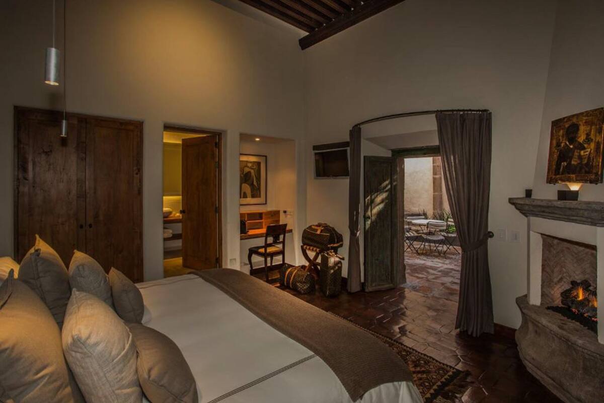 A bedroom with a large bed, a fireplace, and a view of a balcony.
