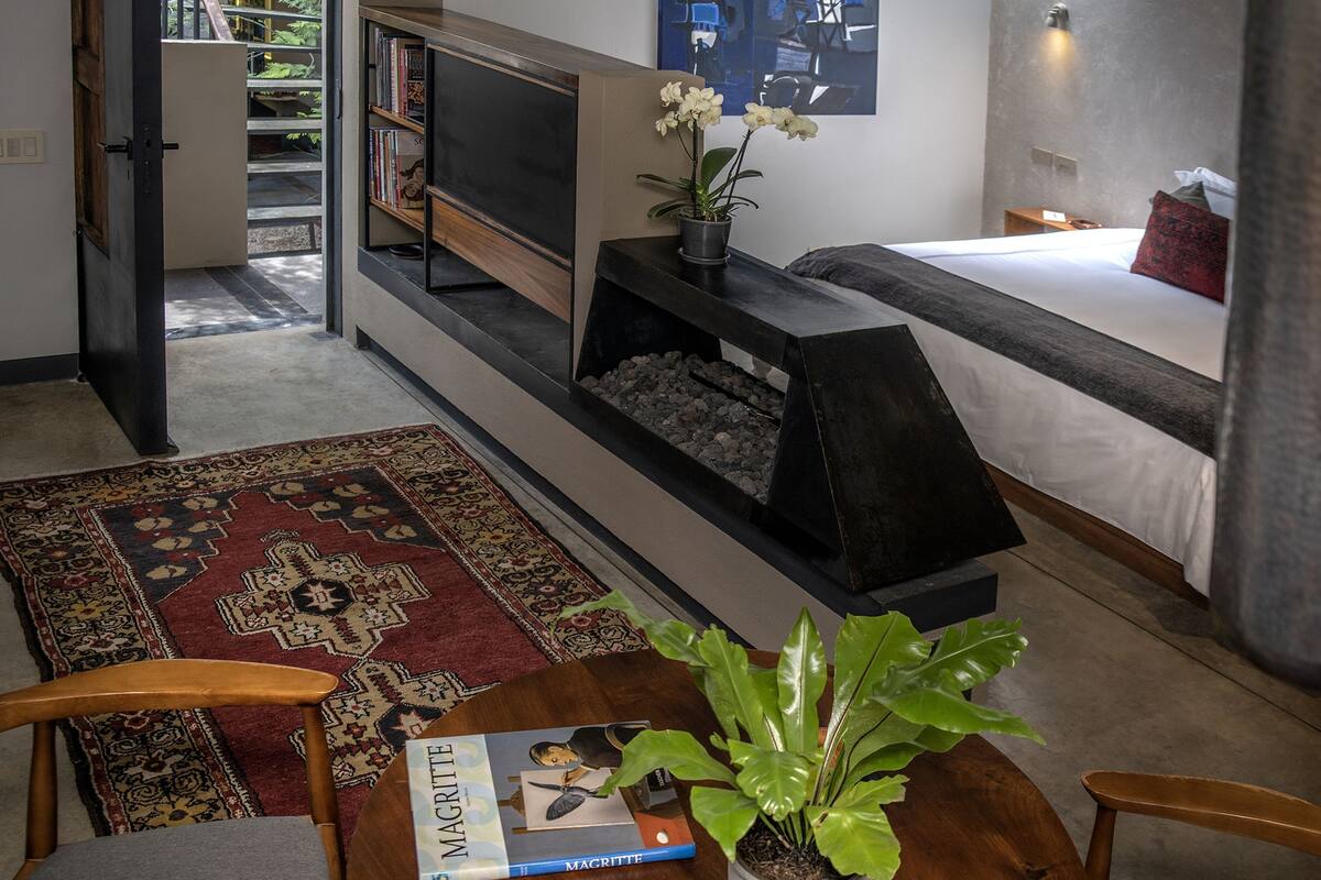 A modern living room with a flat-screen TV, a bookshelf, a fireplace, a bed, and a dining area with a table and chairs.