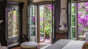 Une chambre à coucher avec un grand lit, une armoire en bois et une vue sur un jardin, accessible par des portes ouvertes.