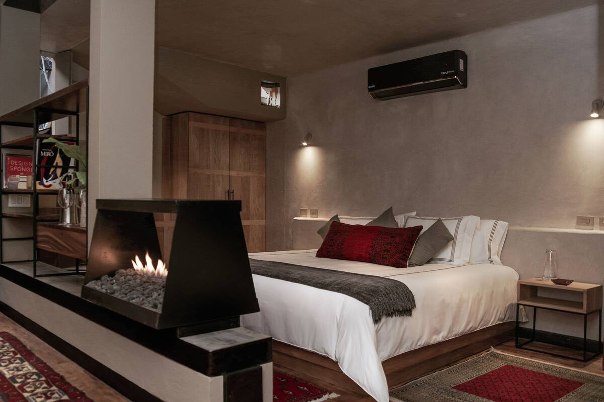 A modern bedroom with a bed, bedside tables, a fireplace, and a wall-mounted air conditioner.