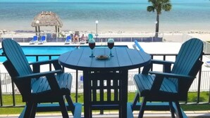 A deck with a table and chairs overlooking a beach with a pool and a palm tree. - Oceanfront oasis beach views heated pool U34 (Marathon)