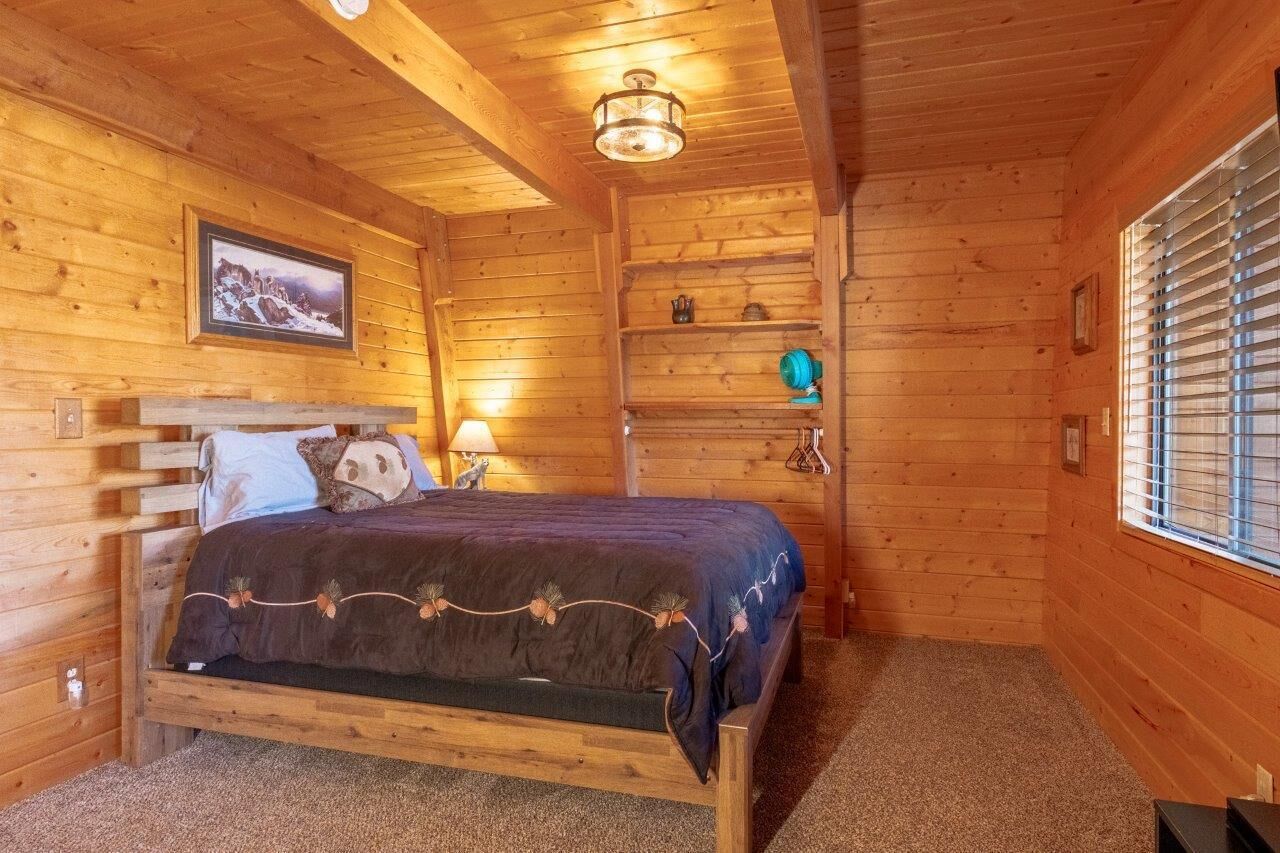 A wooden cabin room with a bed, a shelf with decorative items, and a window with blinds.