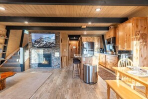 A modern kitchen with wooden cabinetry, a stone fireplace, and a dining area with a wooden table and chairs. - Wolf Hollow - Serene, Cozy Cabin Located 31 miles from YNP with A/C and hot tub (Island Park)