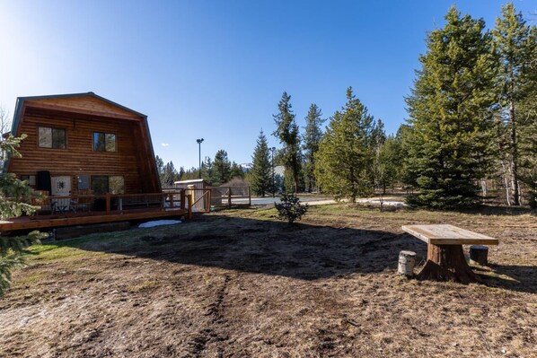 A rustic wooden cabin with a deck, surrounded by a forest and a clear sky. - Wolf Hollow - Serene, Cozy Cabin Located 31 miles from YNP with A/C and hot tub (Island Park)