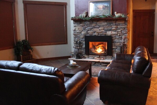 A cozy living room with a stone fireplace, leather sofas, and a coffee table.