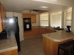 A kitchen with wooden cabinets, a black refrigerator, a built-in oven, a coffee maker, and a window with blinds.