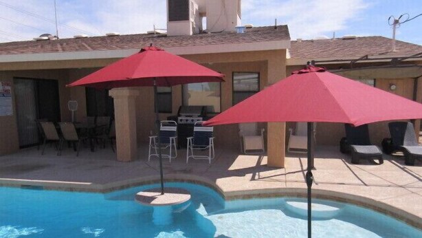 Uma piscina com guarda-sóis vermelhos, espreguiçadeiras e espaço para churrasco.